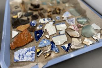 Tray containing archaeological artifacts, including ceramic sherds, glass fragments, and other excavated materials.