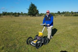 Researcher operating ground-penetrating radar equipment in an open field during archaeological survey work.